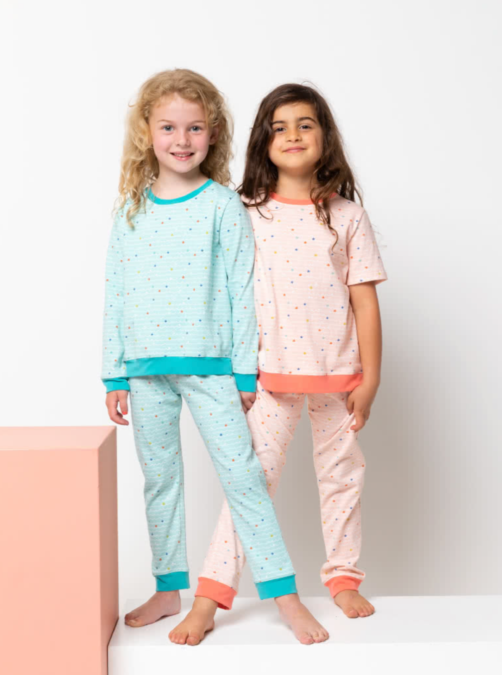Children wearing the Baby/Child PJ Set sewing pattern from Style Arc on The Fold Line. A pyjamas pattern made in knit jersey fabrics, featuring a pyjama top with long or short sleeves, crew neck, cuffs and hem band. Pyjama pant has elastic waist and cuff 