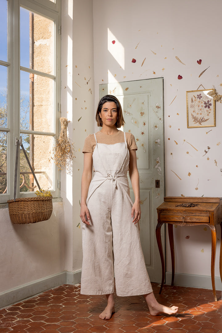 Woman wearing the Pablo Overall sewing pattern from Ready To Sew on The Fold Line. An overall/apron combo pattern made in linen, or ramie, fabrics, featuring a wrap around the hips and waist feature, relaxed fit, two front and four back darts, wide legs, 