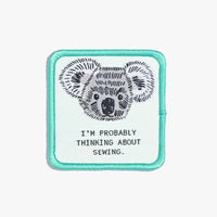 Photo of the ‘I’m Probably Thinking About Sewing’ iron-on patch from Kylie & The Machine on The Fold Line. A square patch featuring a koala with a mint green background and border ready to be attached to your handmade garment or bag.