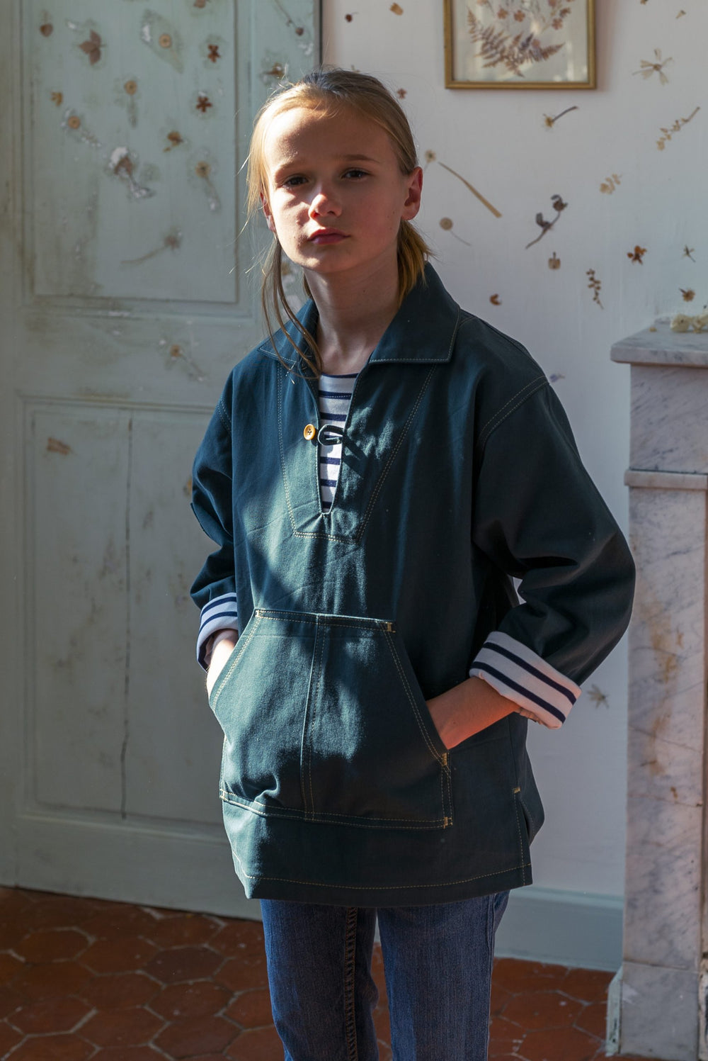Child wearing the Paulin Smock sewing pattern from Ready to Sew on The Fold Line. A jacket pattern made in light to heavyweight denim, or cotton canvas fabrics, featuring a split collar with single button closure, two front patch pockets, loose fit, singl