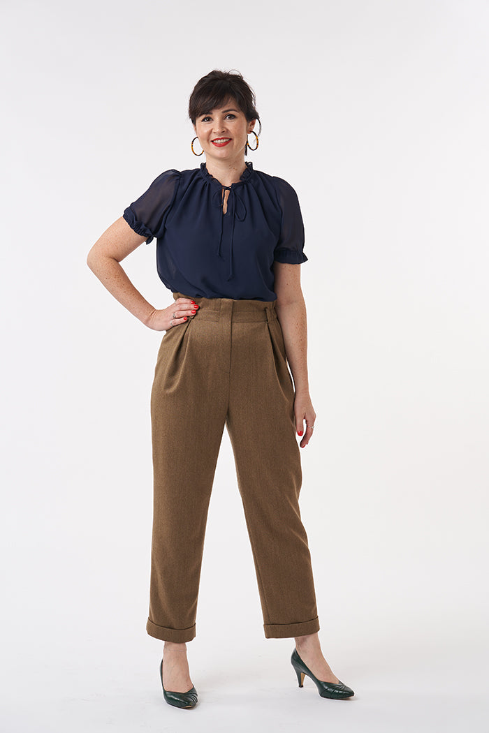 Woman wearing the Peggy Trousers sewing pattern from Sew Over It on The Fold Line. A trouser pattern made in wool, wool suiting, linen or heavy weight crepe fabrics, featuring a high paper bag waist, zip fly, elasticated around the side and back waist, fr