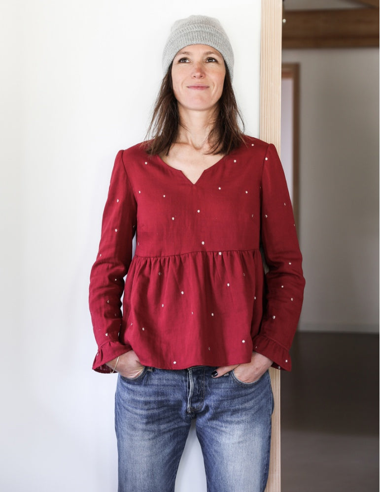 Woman wearing the Pepa Blouse sewing pattern from Atelier Scämmit on The Fold Line. A blouse pattern made in batiste, crepe, double gauze, or light denim fabrics, featuring a round neckline with small V notch, button back closure, long sleeves with gather