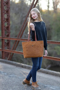 Woman holding the Pepin Tote sewing pattern from Noodlehead on The Fold Line. A tote pattern made in canvas or waxed canvas fabrics, featuring a front pocket with snap closure, divided interior pocket, recessed zip closure and shoulder length straps.