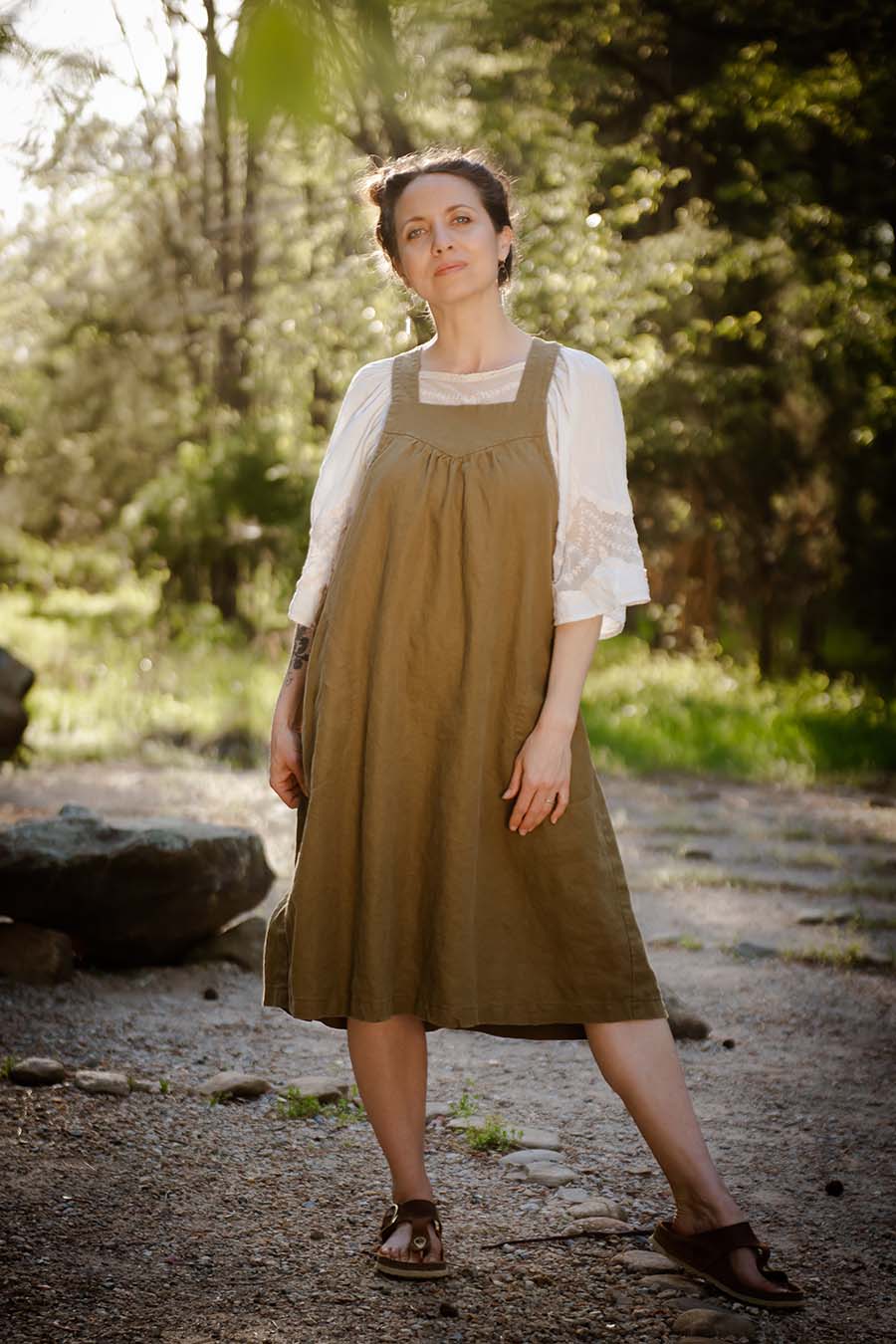 Woman wearing the Petrichor Pinafore sewing pattern from Sew Liberated on The Fold Line. A pinafore dress with a yoke, gathers, and deep pockets.