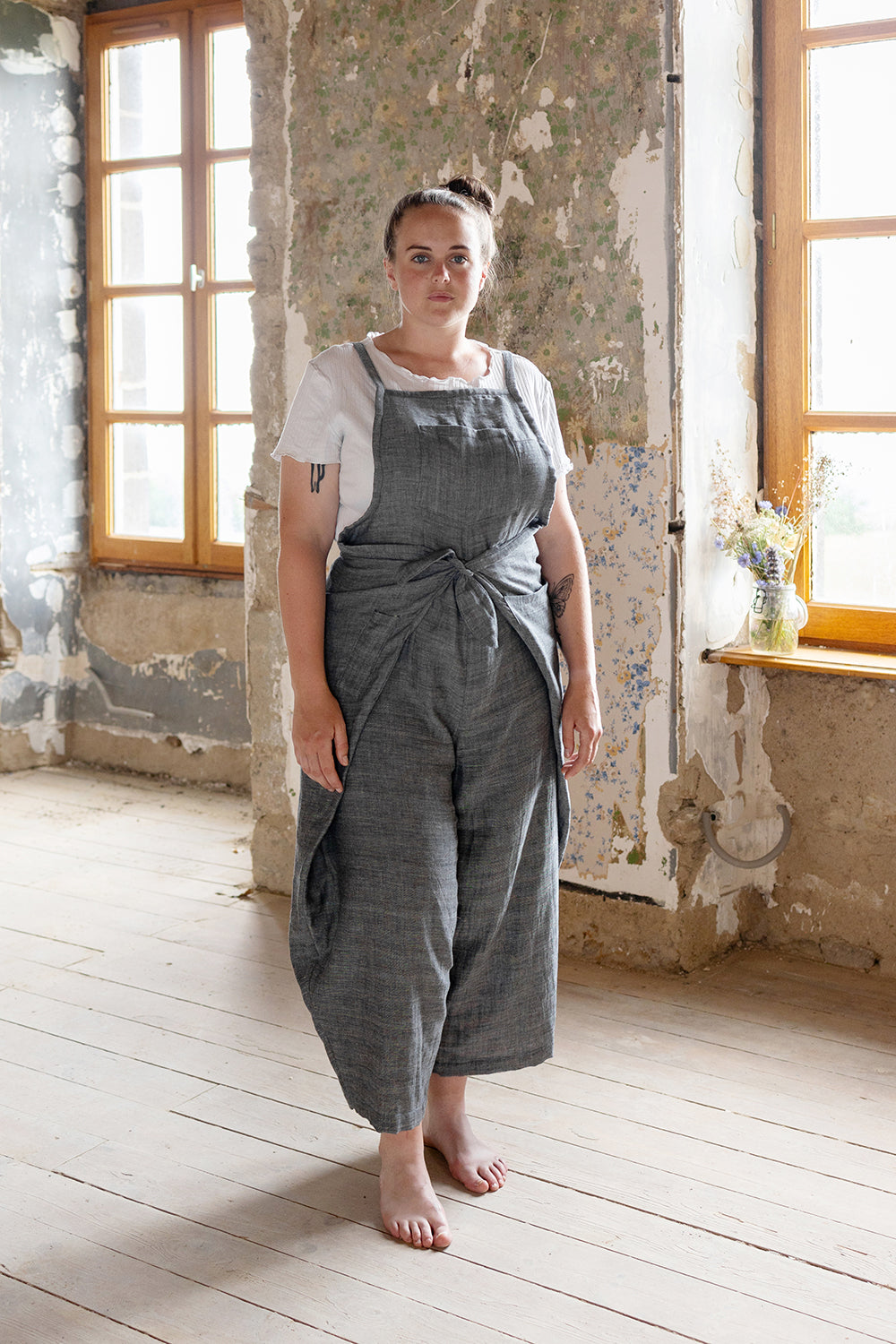 Woman wearing the Pincha Overalls sewing pattern from Ready to Sew on The Fold Line. An overalls/apron combo pattern made in linen or ramie fabrics, featuring a wrap around your hips and waist style, bow tie at front waist, balloon legs, five patch pocket