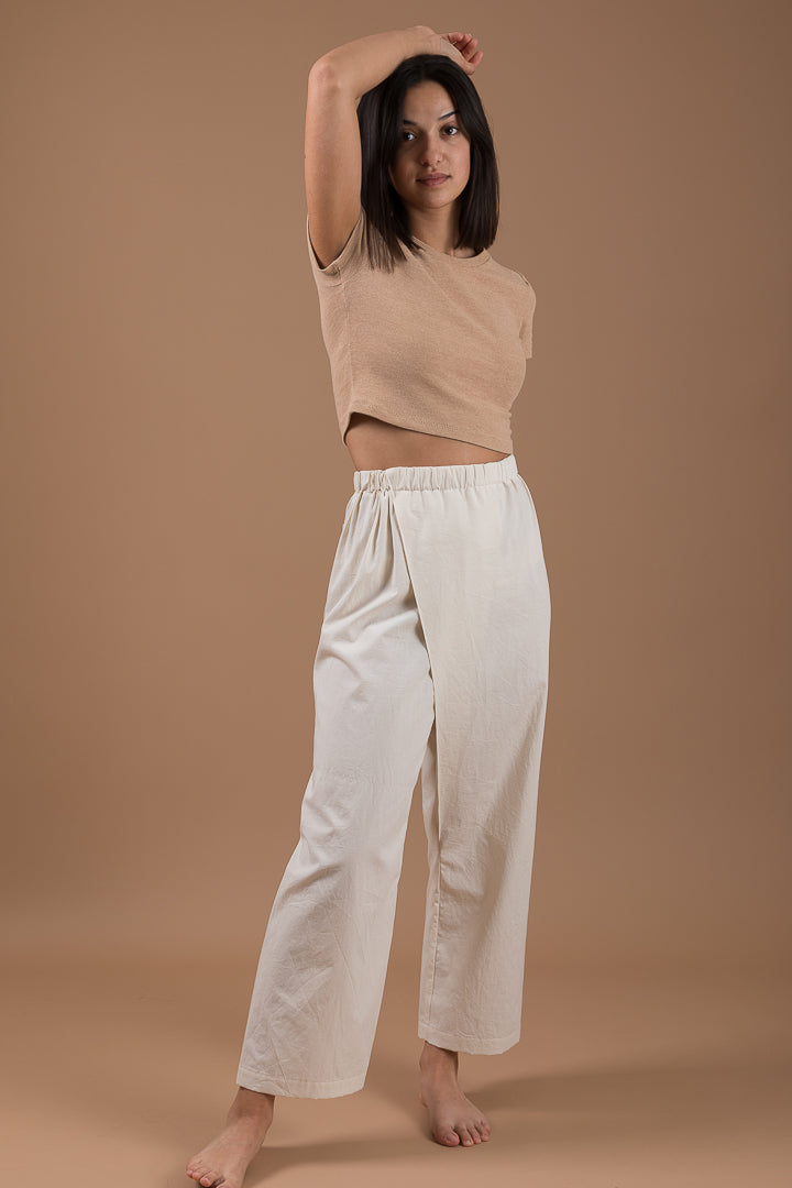 Woman wearing the Pleat Asymmetrical Pants sewing pattern from Ready to Sew on The Fold Line. A trouser pattern made in cotton poplin, linen, batik or light denim fabrics, featuring a straight-leg, high elasticated waist, slightly cropped leg and overlapp