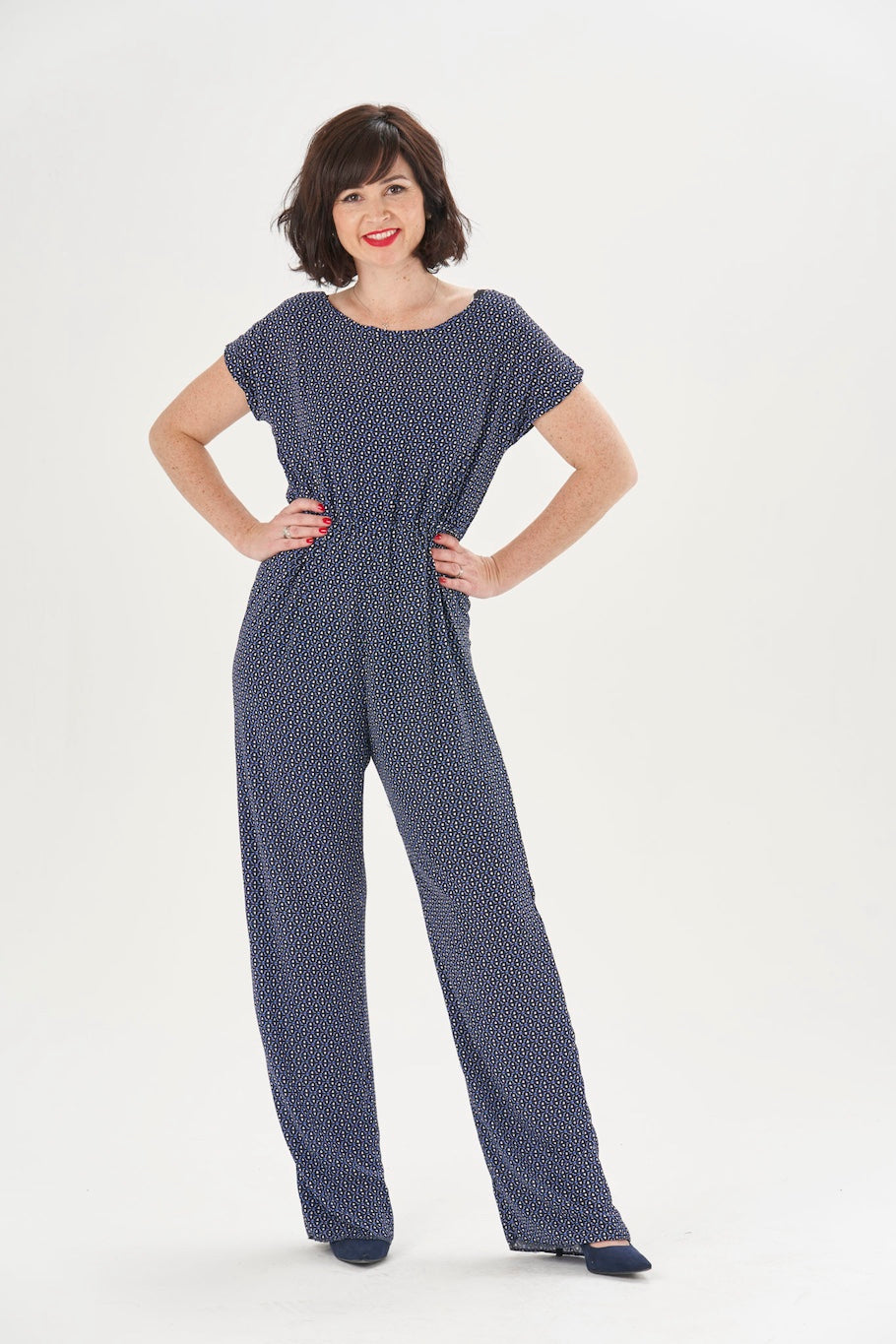 Woman wearing the Poppy Playsuit sewing pattern from Sew Over It on The Fold Line. A jumpsuit pattern made in rayon, viscose or crepe fabrics, featuring a relaxed fit, wide neckline, grown-on sleeves, keyhole back opening, elasticated waist, and full-leng