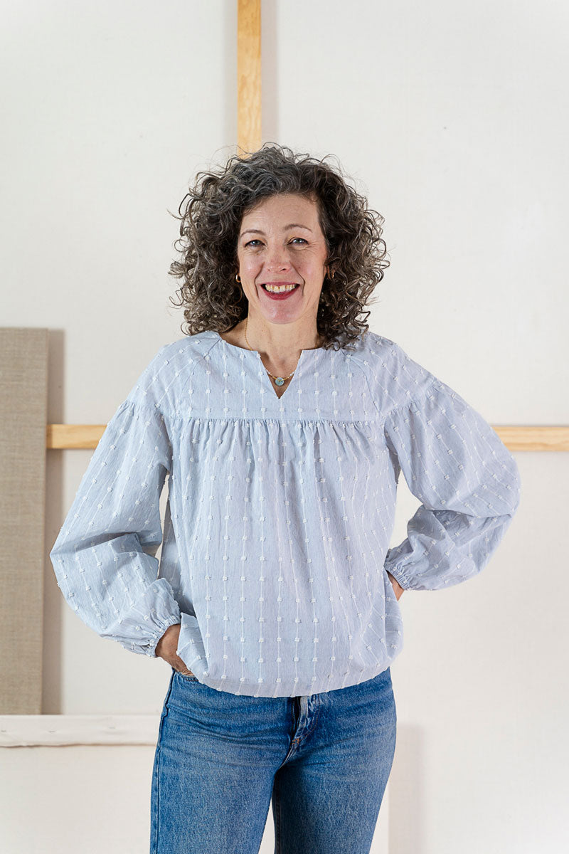 Woman wearing the Positano Blouse sewing pattern from Liesl + Co on The Fold Line. A peasant blouse pattern made in cotton voile, lawn, poplin, chambray, linen, or rayon fabric, featuring full, gathered raglan sleeves with elastic cuffs, a V-neck notch, a