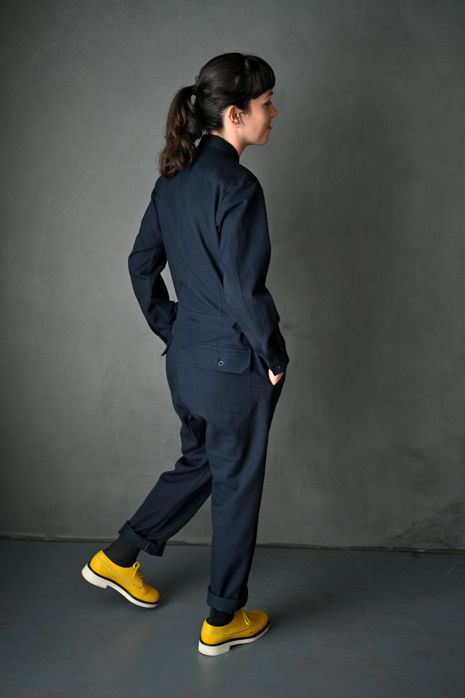 Woman wearing the Thelma Boilersuit sewing pattern by Merchant and Mills. A boilersuit pattern made in twill, denim, cotton poplin or linen fabric featuring a loose fit, back pockets, breast pockets, collard neck, front zip and long sleeves.