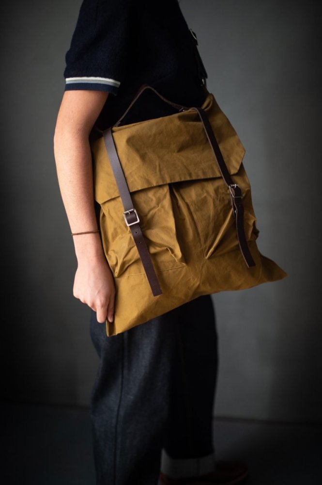 Woman holding the RTR Rucksack sewing pattern from Merchant & Mills on The Fold Line. A bag pattern made in oilskin or sturdy canvas fabrics, featuring a full lining, three divided internal pockets, two external patch pockets, hand strap, shoulder straps,