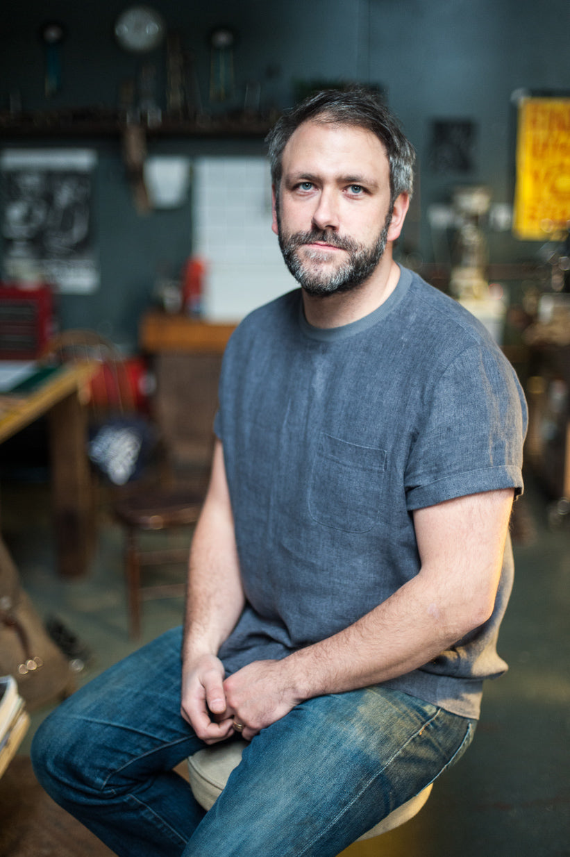 Man wearing the Tee Shirt sewing pattern by Merchant and Mills. A tee pattern made in laundered linens, soft cottons, lightweight denims or soft light wool fabric featuring a stretch rib neck, breast pocket and rolled up sleeves.