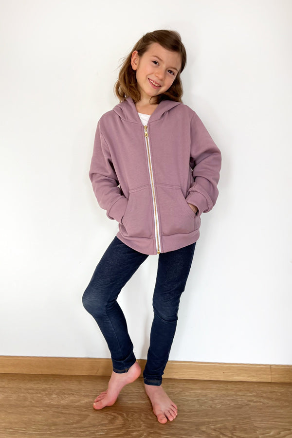 Child wearing the Child/Teen Mini Rainbow Hoodie sewing pattern from I AM Patterns on The Fold Line. A hoodie pattern made in sweatshirt, interlock, neoprene or French terry fabrics, featuring front pockets, front zip closure, full length sleeves, hood, r
