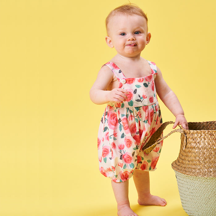 Baby wearing the Babies' Raspberry Romper sewing pattern from Poppy & Jazz on The Fold Line. A romper pattern made in cotton lawn, cotton poplin, linen or broderie anglaise fabrics, featuring inside leg seam popper closure, adjustable straps, bodice and g