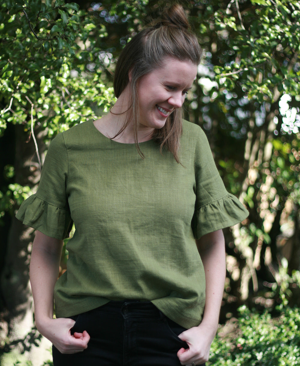 Woman wearing the Rātā Top sewing pattern by Below the Kowhai. A blouse pattern made in light to medium weight cotton, chambray, poly cotton, linen, rayon, sateen or tencel fabrics, featuring a round neckline, button and loop back closure and a sleeve ruf