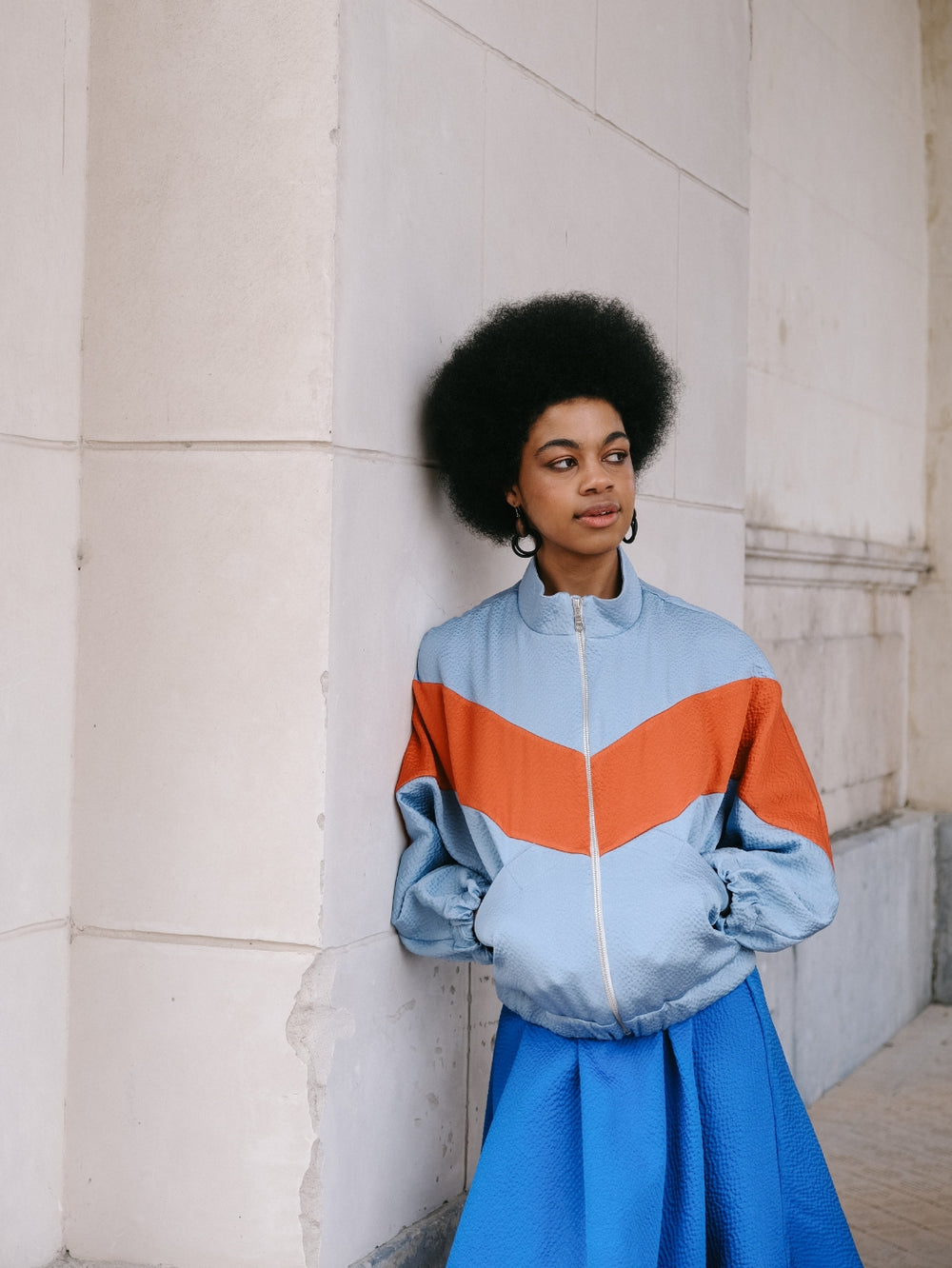 Woman wearing the Rava Jacket sewing pattern from Notches on The Fold Line. A jacket pattern made in jersey, sweatshirt, french terry, ponte, thin nylon, or wool fabric, featuring a retro 80s vibe, diagonal seamlines, pockets, grown-on sleeves, and a zip 