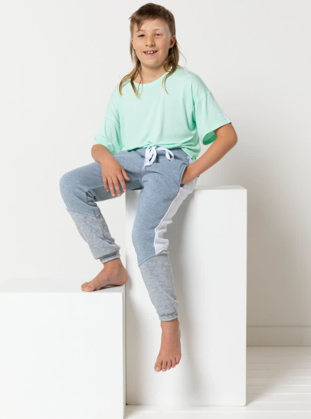 Child wearing the Child/Teen Riley Sweatpant sewing pattern from Style Arc on The Fold Line. A sweatpant pattern made in fleece, jersey, or sweater knit fabrics, featuring an elasticated waist and cuffs, non-functional shoelace waist tie, in-seam pockets,