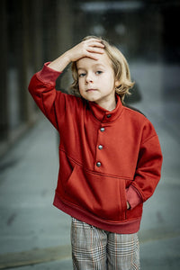 Child wearing the Child/Teen Robin Pullover sewing pattern from Fibre Mood on The Fold Line. A jumper pattern made in French terry, sweatshirt or jacquard fabrics, featuring an oversized fit, standing collar, front snap closure, kangaroo pocket, ribbed wr