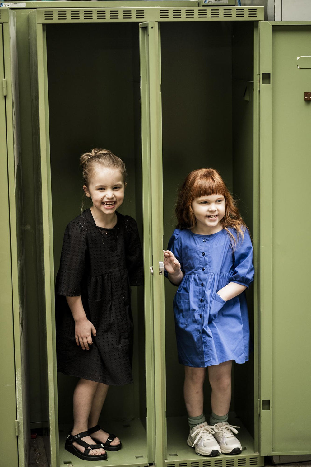 Children wearing the Child/Teen Rosa Dress sewing pattern from Fibre Mood on The Fold Line. A dress pattern made in Knit fabrics, featuring patch pockets, front button closure, waist gathers, shoulder gathers, and at the top and bottom of the sleeve, thre
