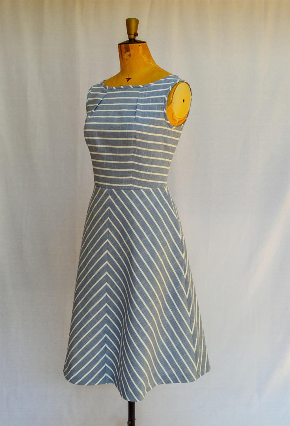 Mannequin wearing the Barcelona Dress sewing pattern from Maven Patterns on The Fold Line. A sleeveless dress pattern made in light to medium weight woven fabrics, featuring a boat neck, fitted at the waist with an A-line skirt, in-seam pockets, front and