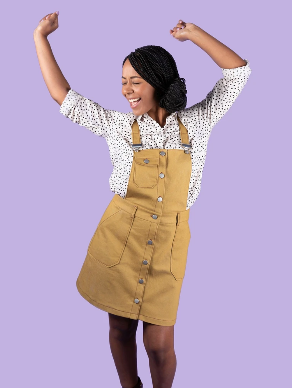 Woman wearing the Bobbi Pinafore sewing pattern from Tilly and the Buttons on The Fold Line. A pinafore pattern made in denim, corduroy, cotton canvas, drill, gobelin (tapestry), or velvet fabric, featuring a button front, slim-look bib, three pockets, an