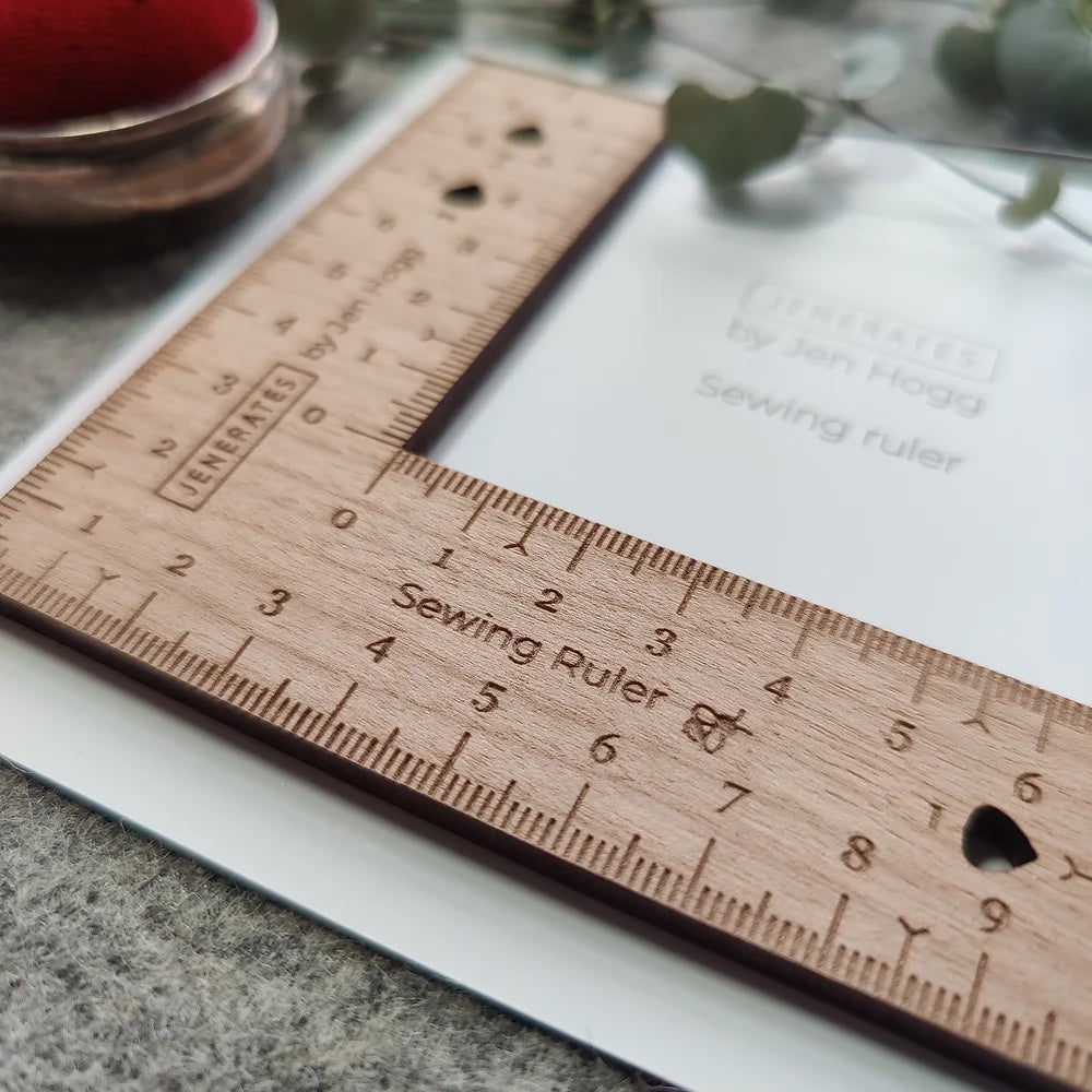 Photo of the Sewing Ruler from Jenerates on The Fold Line. A useful square ruler made in cherry wood veneer and marked in centimetres or inches with cut outs for adding or subtracting seam and hem allowances.