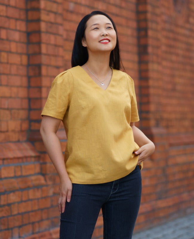 Woman wearing the Seychelles Top sewing pattern by Itch to Stitch. A top pattern made in linen’s, rayon challis, charmeuse, lawn, chambray, poplin or sateen fabrics, featuring a short sleeve with pleats, button and loop back closure and V-neck.