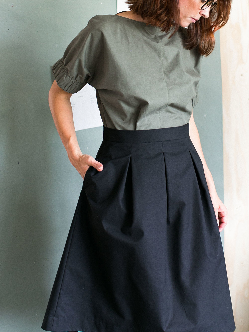 Woman wearing the Three Pleat Skirt sewing pattern by The Assembly Line. A pleated skirt pattern made in denim, cotton twill or canvas fabric featuring a right side pocket, and left side zipper opening.