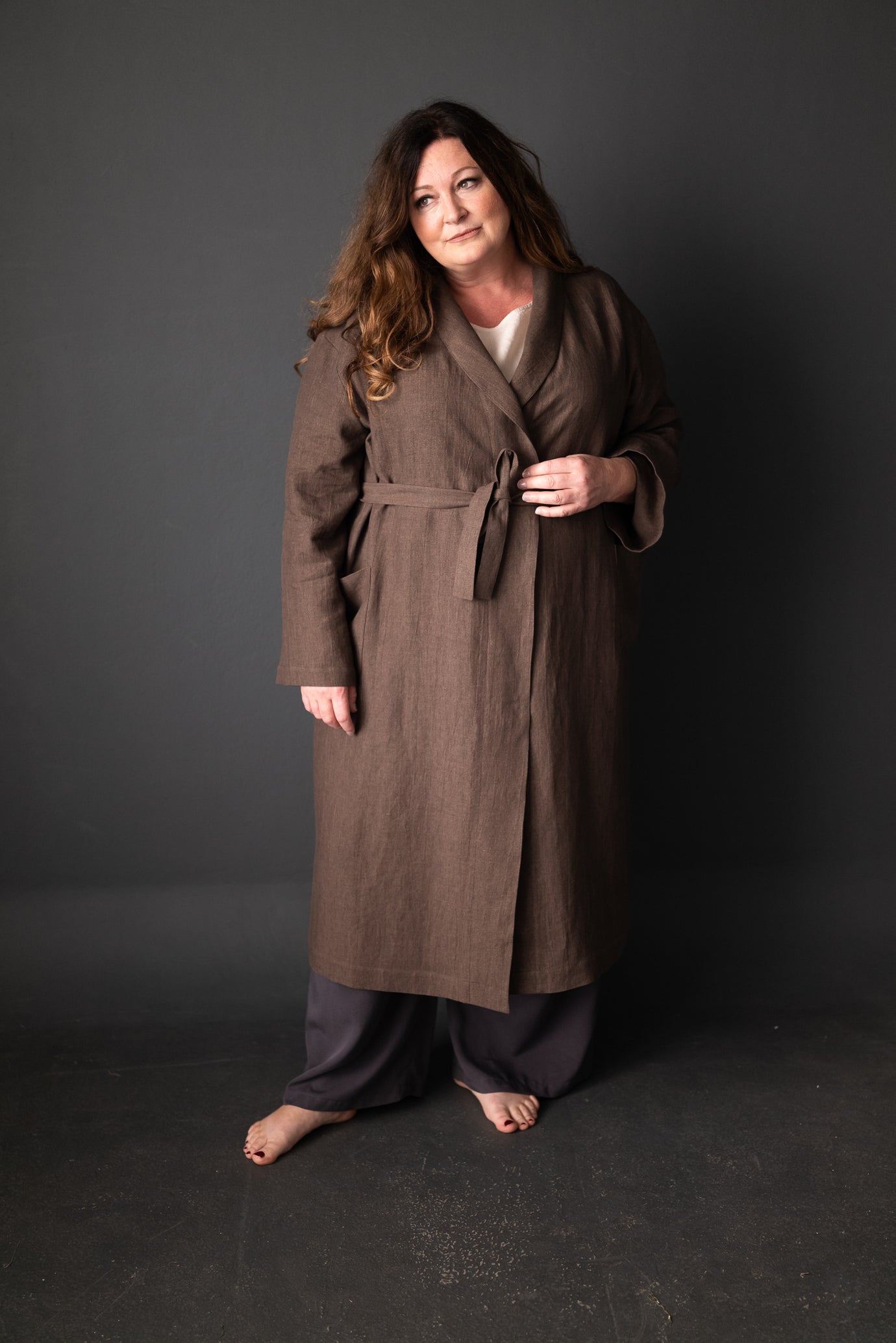 Woman wearing the Unisex Sunday Robe pattern from Merchant and Mills on The Fold Line. A robe pattern made in linen, cottons, lawn, linen waffle or tencel/linen fabrics, featuring an inner tie, patch pockets, shawl collar, self-fabric tie belt and mid-cal
