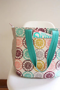 Photo showing the Super Tote sewing pattern from Noodlehead on The Fold Line. A tote bag pattern made in heavy linen, denim, canvas or twill fabrics, featuring a generous size, recessed zip closure, roomy interior pockets, front exterior pocket, piping an