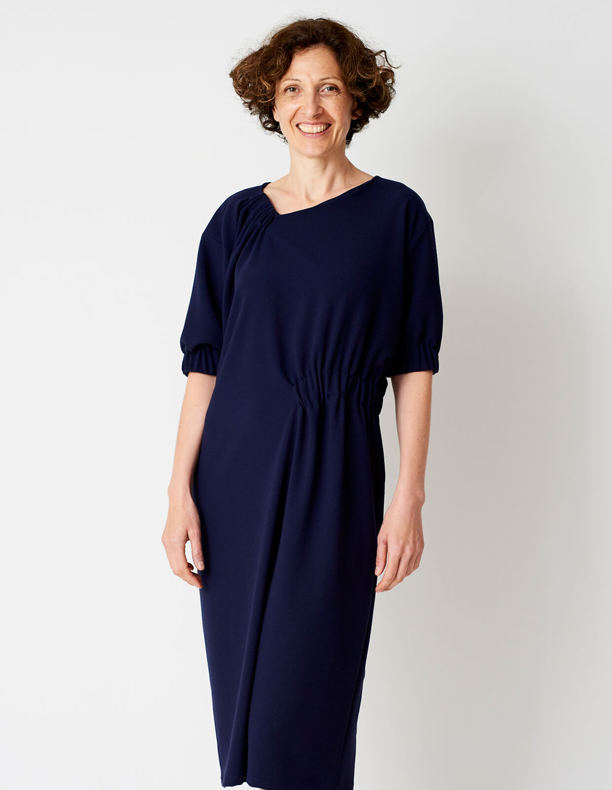 Woman wearing the Asymmetric Gather Dress sewing pattern from The Maker's Atelier on The Fold Line. A dress pattern made in wool or poly/viscose mixes, wool or silk crepes, and silk satins fabrics, featuring an off-center V-neck, relaxed fit, elbow length