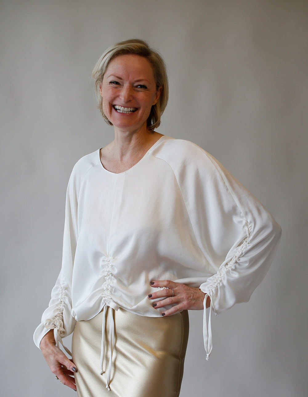 Woman wearing Tie Detail Top sewing pattern from The Maker's Atelier on The Fold Line. A blouse pattern made in tencel, viscose, silks, or soft cotton fabrics, featuring bat wing raglan sleeves, ruched gathers on the front and sleeves, round neck and rela