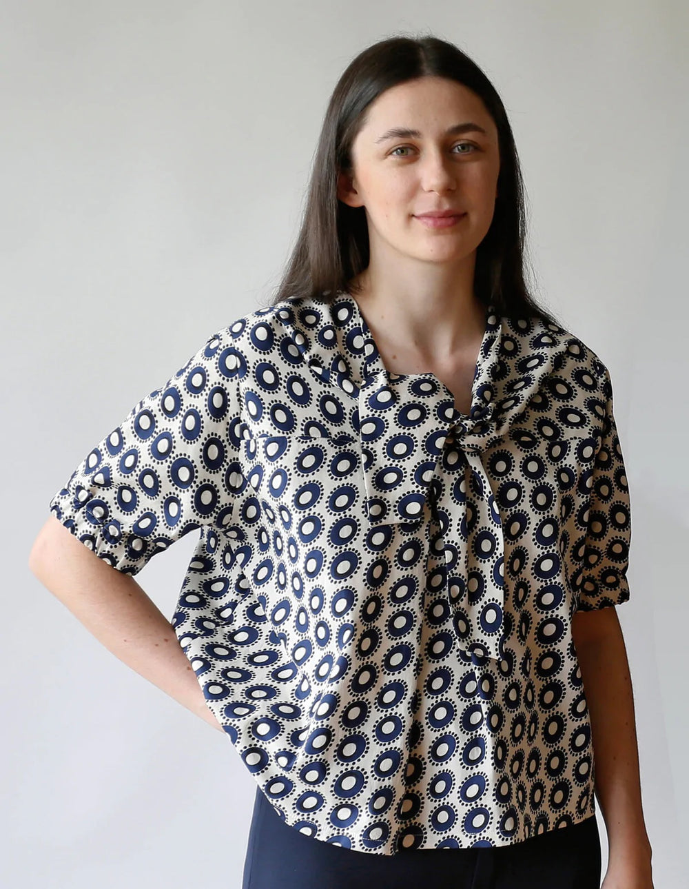 Woman wearing the Tie Blouse sewing pattern from The Maker's Atelier on The Fold Line. A blouse pattern made in fine count cotton, Tana lawn, silk, tencel, or viscose fabrics, featuring a pull-on style, relaxed fit, elbow length sleeves, front neck tie, f