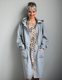 Woman wearing the Utility Coat sewing pattern from The Maker's Atelier on The Fold Line. A coat pattern made in linens, parachute silks, coated or waxed cottons, lightweight waterproof fabrics and oilskins fabrics, featuring a relaxed fit, unlined, hood, 