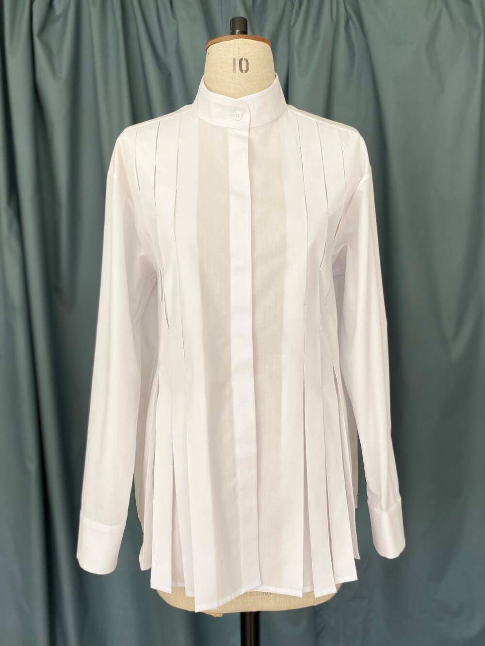 Mannequin wearing the TPCSH2 Box Pleat Shirt sewing pattern from Trend Patterns on The Fold Line. A shirt pattern made in crisp or floaty cotton fabrics, featuring a straight silhouette, front box pleats, concealed button placket, shirt style sleeve, boun