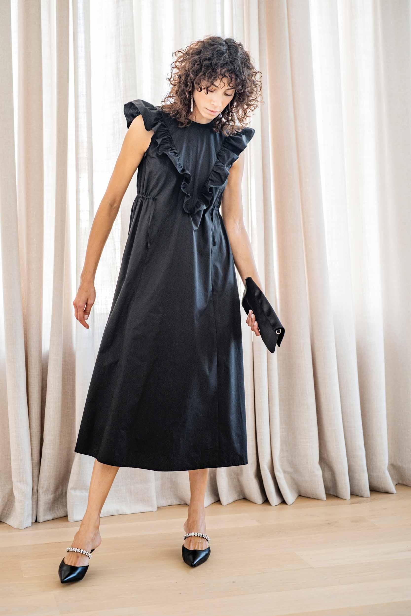 Woman wearing the Tammy Dress sewing pattern from Fibre Mood on The Fold Line. A dress pattern made in woven viscose, chambray, fine wale corduroy, velvet, poplin, broderie anglaise, or lyocell fabrics, featuring a A-line cut, V-shaped ruffled bodice, sid