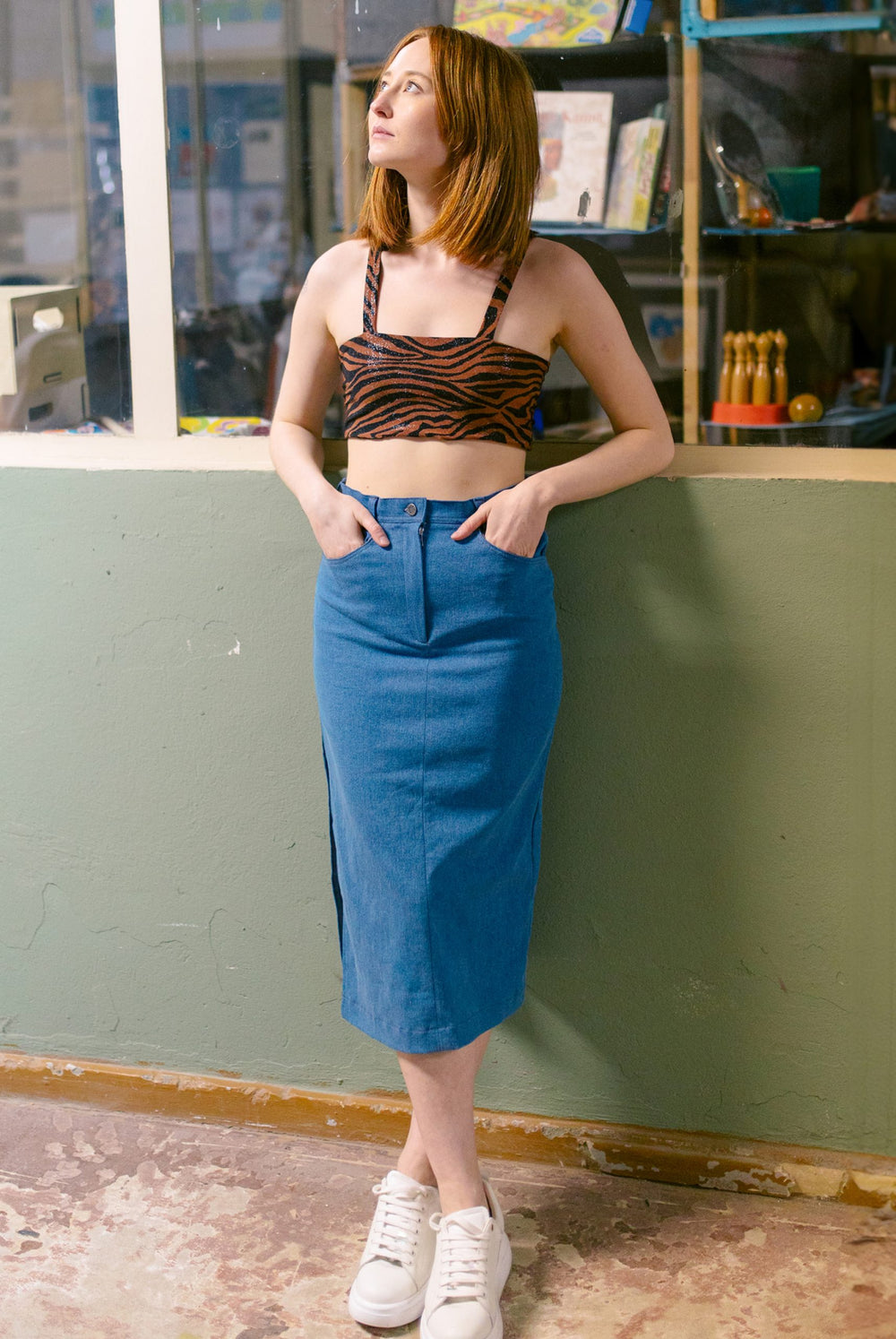 Woman wearing the Frida Skirt sewing pattern from JULIANA MARTEJEVS on The Fold Line. A denim skirt pattern made in stretch denim fabrics, featuring a midi length, straight silhouette, fly front closure, pockets, topstitching, and high slit in the side se