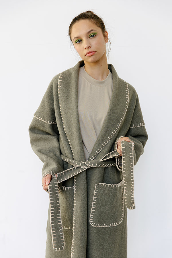 Woman wearing the Kelly Coat sewing pattern from JULIANA MARTEJEVS on The Fold Line. A hand sewn coat pattern made in wool loden fabrics, featuring a midi length, wrap closure, belt, shawl collar, back vent, patch pockets, using only a simple hand embroid