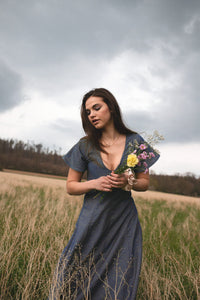 Woman wearing the Rory Dress sewing pattern from JULIANA MARTEJEVS on The Fold Line. A dress pattern made in linen, cotton, or light denim fabrics, featuring a midi length, deep v-neckline, flared short sleeves and flared skirt.