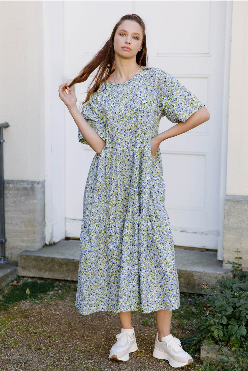 Woman wearing the Utah Dress sewing pattern from JULIANA MARTEJEVS on The Fold Line. A dress pattern made in cotton poplin fabrics, featuring a loose fit, wide elbow length sleeves, gathered tiers, midi length, side pockets, and tie closure at back neckli