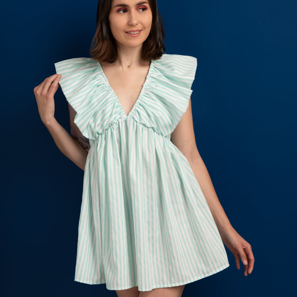 Woman wearing the Olivet Dress sewing pattern from Madalynne on The Fold Line. A dress pattern made in cotton, chambray, or linen fabric, featuring exaggerated ruffles over the shoulders, a deep V-neckline, gathered skirt, and mini length.