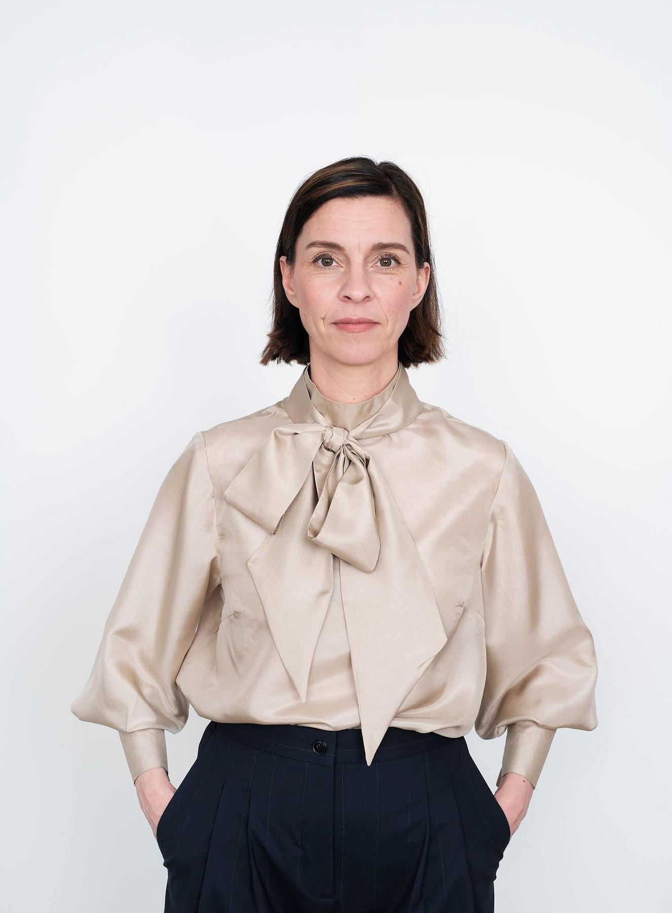 Woman wearing the Tie Bow Blouse sewing pattern by The Assembly Line. A blouse pattern made in cotton, silk, lawn, linen, crepe de chine or wool crepe fabrics, featuring, bust darts, a standing collar to which you can attach a tie with buttons at the back