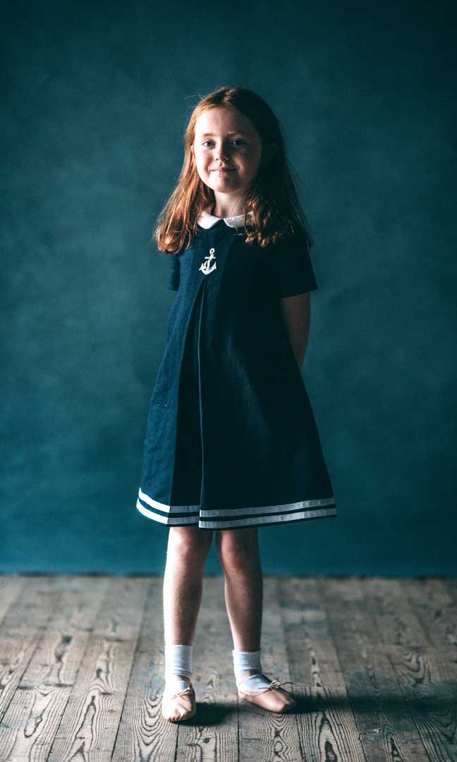 Child wearing the Tilly-pom Dress sewing pattern from Sew La Di Da Vintage on The Fold Line. A playsuit pattern made in linen, denim, chambray, stretch cottons, cottons and prints, velvet, or taffeta fabrics, featuring a peter pan collar, round neckline, 