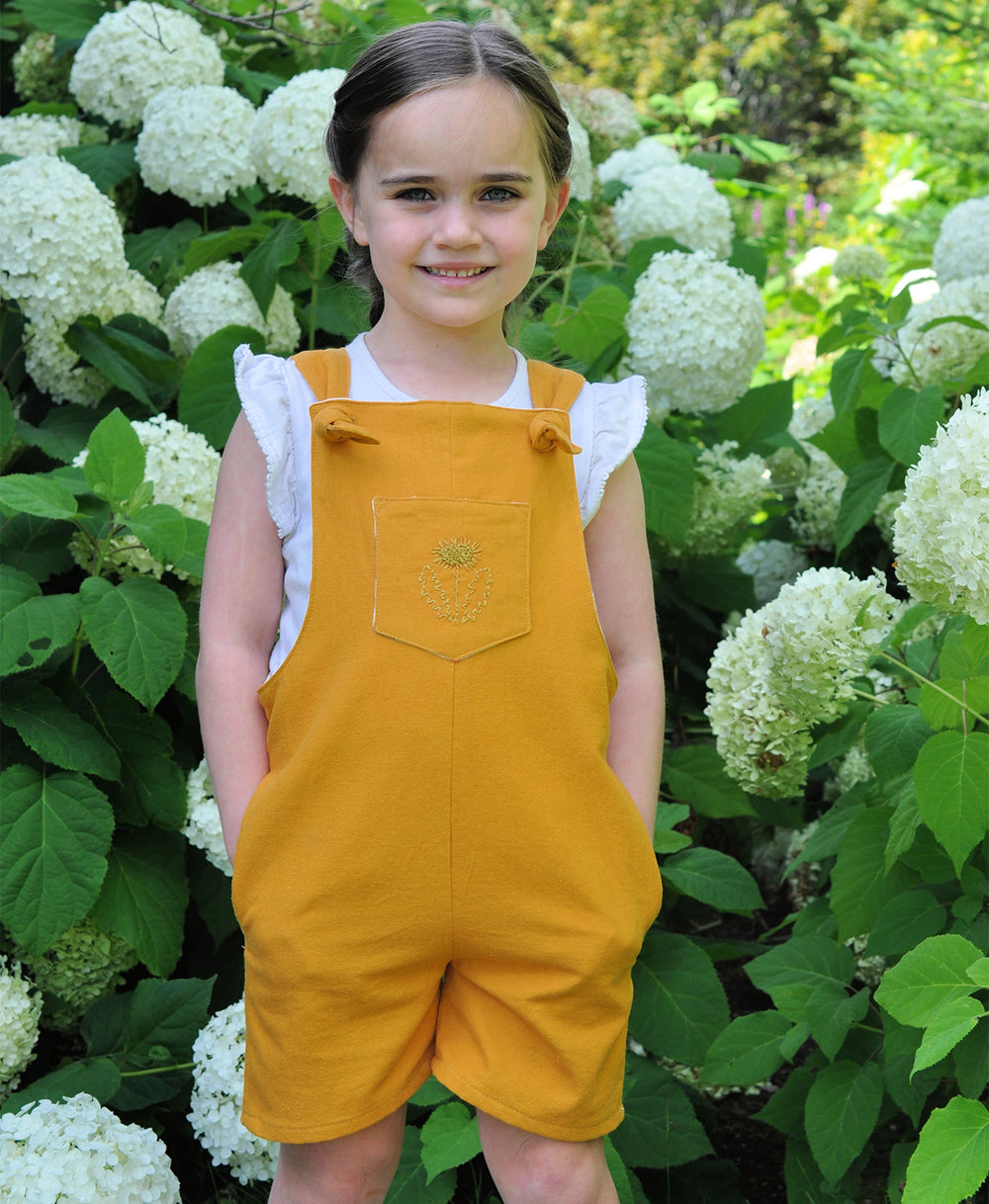 Child wearing the Baby/Child Tipa Dungarees sewing pattern by Below the Kowhai. A sleeveless dress pattern made in light to medium weight cotton, chambray, linen, or medium to heavy weight denim, drill or twill fabrics, featuring cross over back straps an