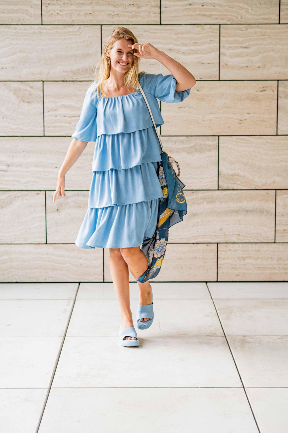 Woman wearing the Trix Dress sewing pattern from Fibre Mood on The Fold Line. A dress pattern made in (viscose) crêpe, lyocell, double gauze, mousseline or chambray fabrics, featuring 4 ruffled tiers, knee length, gathered rectangular neckline, elbow leng