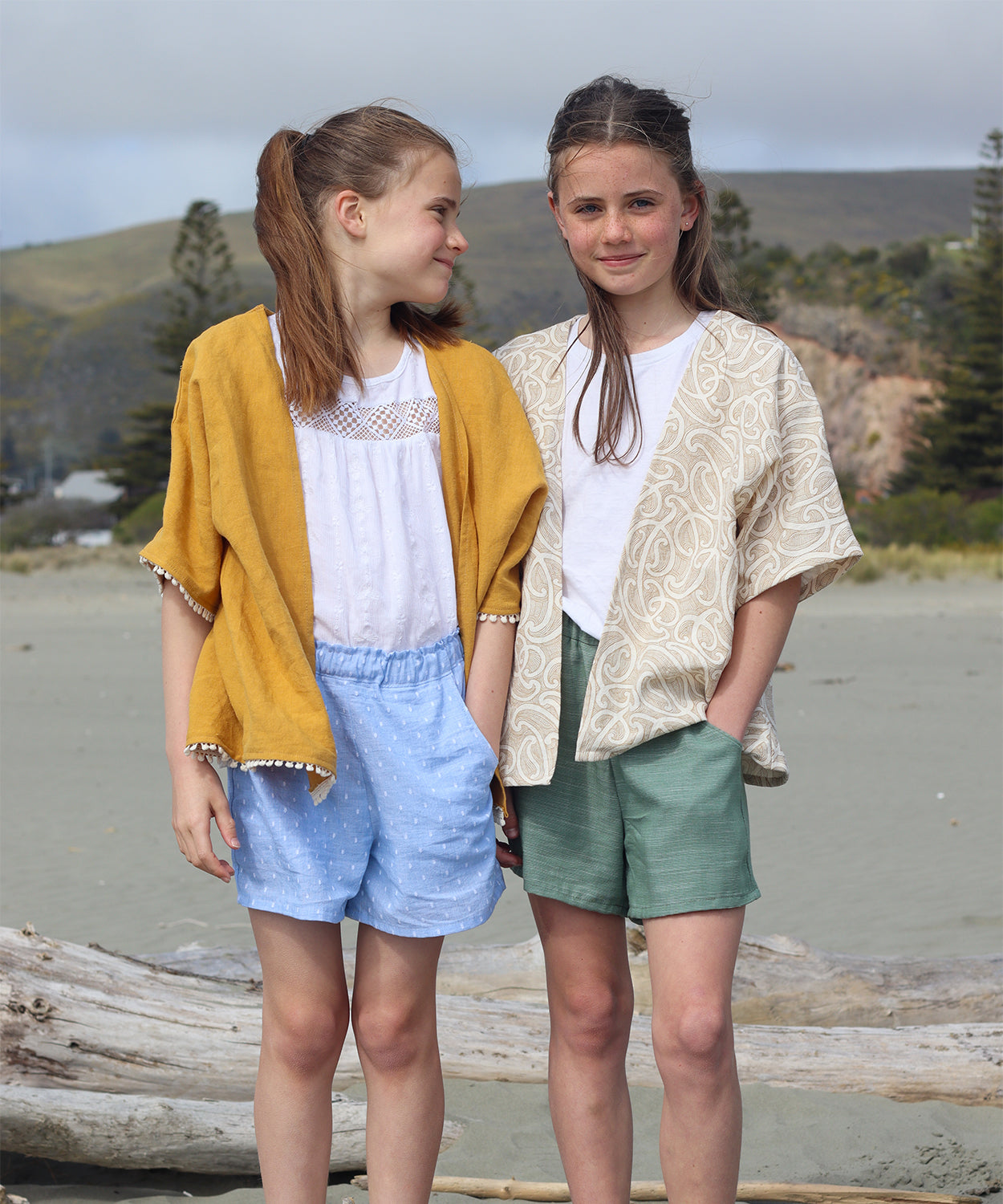 Children wearing the Baby/Child/Teen Tuatua Cover Up sewing pattern from Below the Kōwhai on The Fold Line. A cover up/jacket pattern made in cotton, poly cotton, linen, chambray or tencel fabrics, featuring a boxy shape, relaxed fit, open front, elbow le