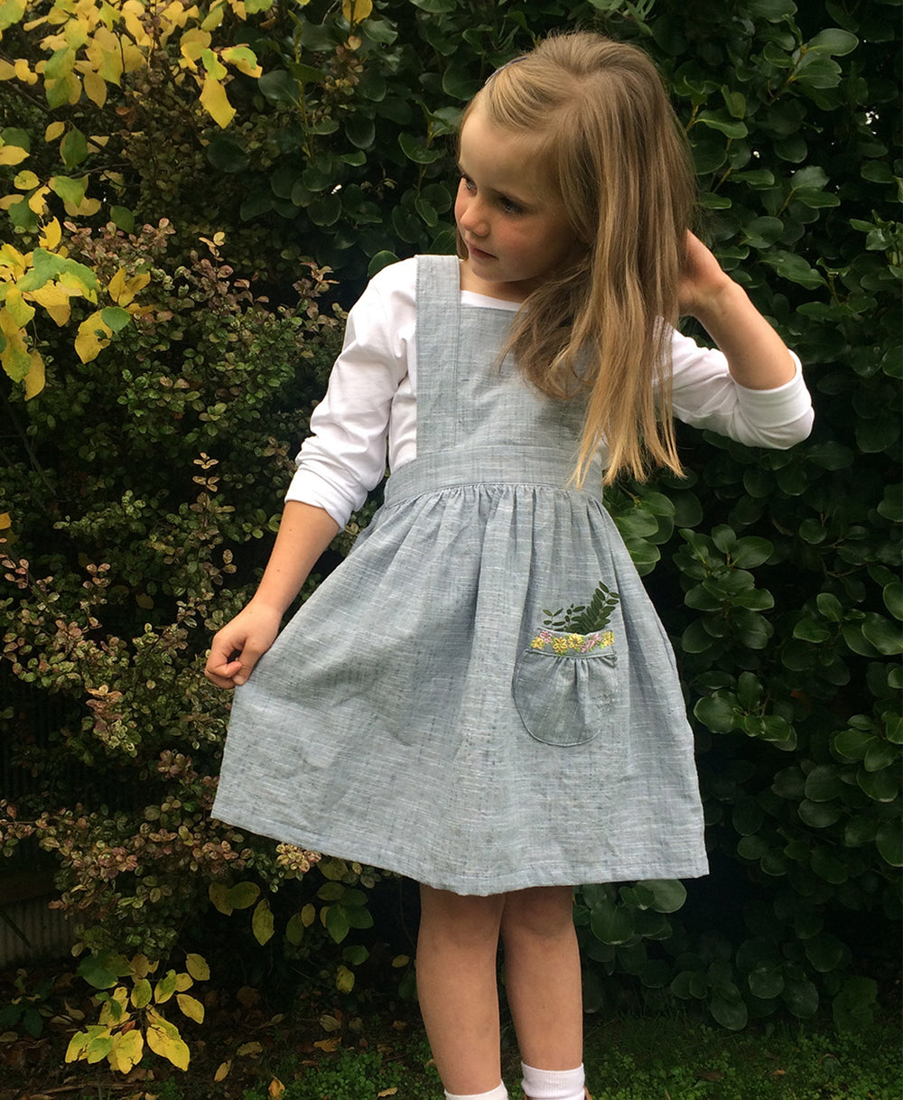 Child wearing the Baby/Child Tui Pinafore sewing pattern by Below the Kowhai. A pinafore dress pattern made in light to medium weight cotton, chambray, light denims, linen, corduroy or velvet fabrics, featuring an elastic back waistband, fully lined bodic