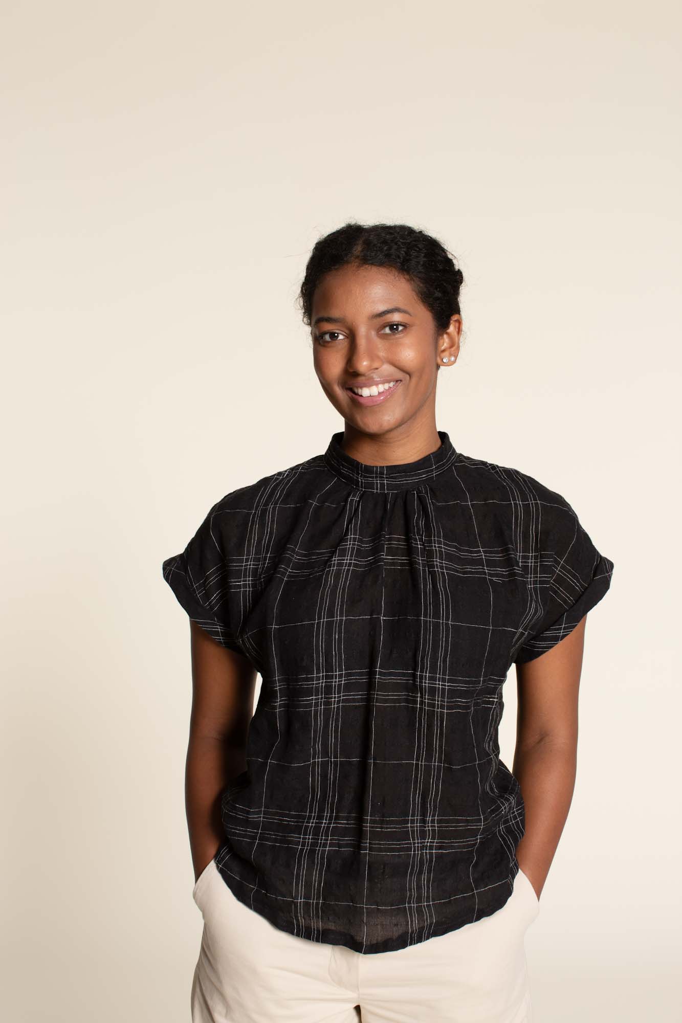 Woman wearing the Tulip Top sewing pattern from Wardrobe by Me on The Fold Line. A top pattern made in cotton, silk or viscose fabrics, featuring short cuffed dolman sleeves, a curved hem, and neckline gathered to the collar.