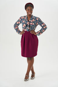 Woman wearing the Tulip sewing pattern from Sew Over It on The Fold Line. A skirt pattern made in medium to heavy weight cotton, wool or crepe fabrics, featuring front slanted pleats, back darts, in-seam pockets, curved side seams, curved waistband, back 