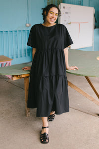 Woman wearing the Utah Dress sewing pattern from JULIANA MARTEJEVS on The Fold Line. A dress pattern made in cotton poplin fabrics, featuring wide elbow length sleeves, gathered tiers, relaxed fit, side pockets, midi length, round neck and back neck tie c