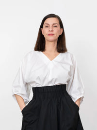 Woman wearing the V-neck Cuff Top sewing pattern from The Assembly Line on The Fold Line. A top pattern made in cotton, silk, lawn, linen, crepe de chine or wool crepe fabrics, featuring a loose fit, V-neckline, and grown-on ¾ length gathered sleeves with
